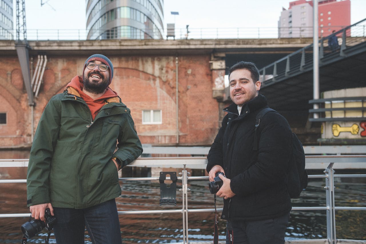 heros-img Two friends with cameras enjoying photography near a river in an urban environment.